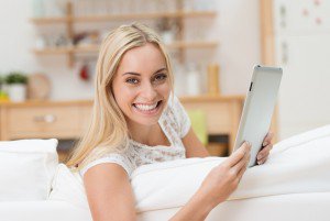 lächelnde junge frau liest tablet auf dem sofa