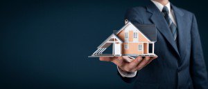 Mann mit Anzug hält Haus in der Hand